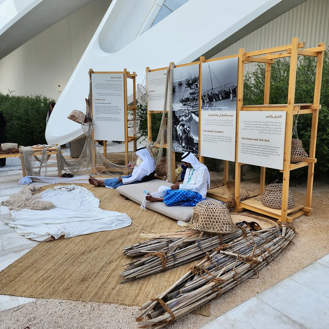 Maritime heritage display featuring palm frond boats, fishing nets, and historical photos at COP28 UAE Pavilion