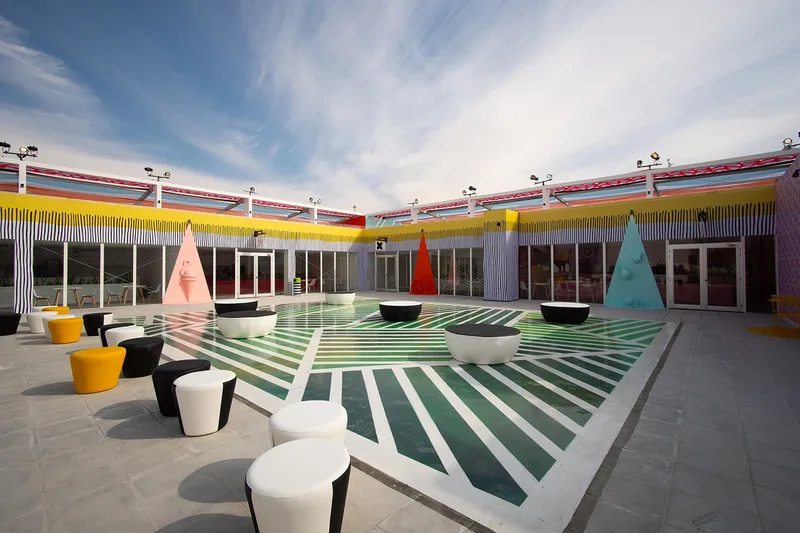 Bright open-air courtyard with geometric floor graphics and modern low stool seating designed by Evolution