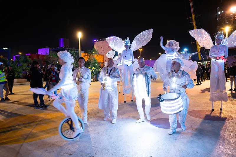 Illuminated illuminated street performers and stilt walkers clad in white wing costumes entertaining crowds at night